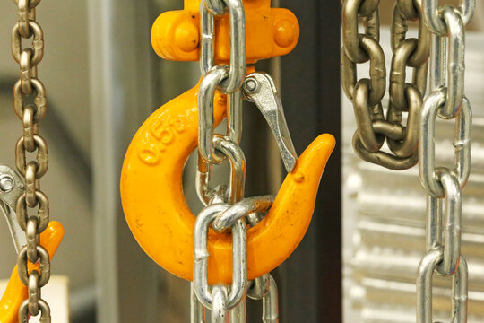 Closeup of a yellow crane hook linked with steel chains, showing industrial lifting gear, hoisting hardware, and heavy duty rigging equipment in a work setting