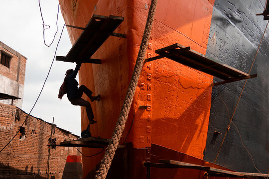Dhaka, Bangladesh - 06 April 2022: View of a worker climbing the hull of a large ship under construction at a shipyard along the Buriganga River.