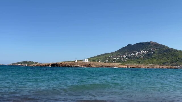 Inquadratura con zoom sulla cappella di Agios Alexandros e sul mulino a vento su un isolotto roccioso vicino alla costa dell'Attica in Grecia