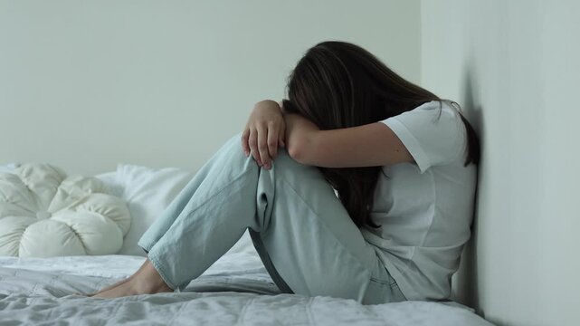 Depressed teenage girl sitting alone on a bed at home, feeling sad and overwhelmed, mental health concept