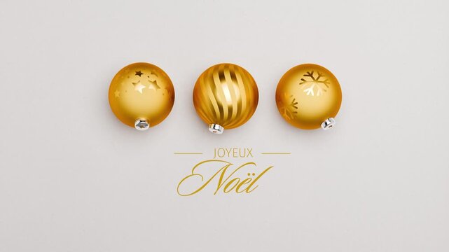 Three golden christmas baubles spinning on a paper surface. French language Merry Christmas messages (Joyeux No&euml;l) appearing and dissolving. Loopable video