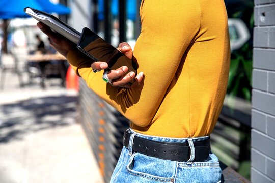 Person in yellow top and jeans holding a tablet outdoors.
