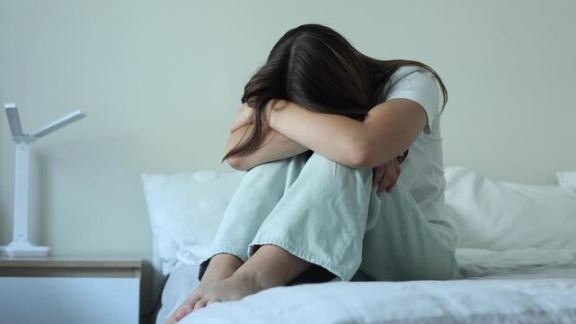 Depressed teenage girl sitting alone on a bed at home, feeling sad and overwhelmed, mental health concept