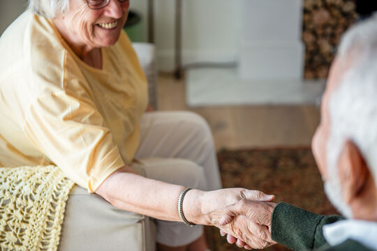 Elderly individuals shaking hands warmly in a cozy living room.