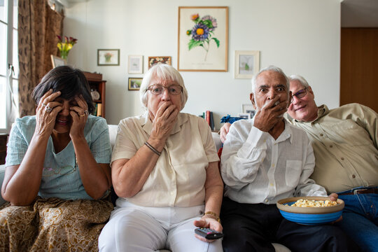 Four elderly people on a couch, surprised while watching TV.