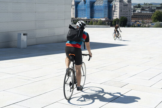 Oslo, Norway - 23 July 2025: View of cyclists riding on the white marble roof of the Oslo Opera House with modern architecture in the background.