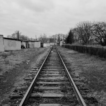 Black and white perspective view of an old railway track passing through an industrial or suburban area with garages and trees