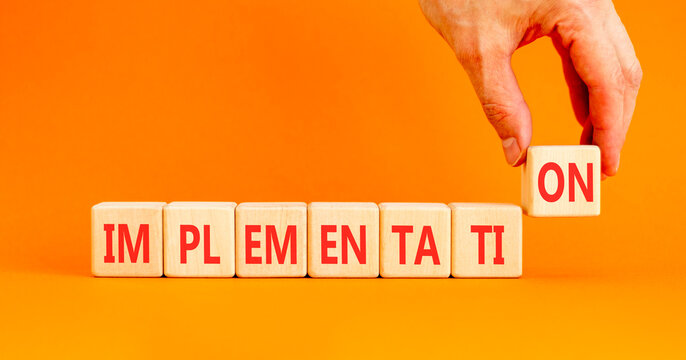 Implementation word symbol. Concept word Implementation on beautiful wooden blocks. Beautiful orange table orange background. Businessman hand. Business implementation word concept. Copy space.