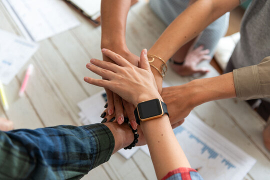 Diverse group of hands stacked in teamwork over a table with papers.