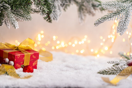 Festive red present with golden ribbon surrounded by gold ornaments, glittering star, and snowy pine branches with soft holiday lights. Winter Christmas Holiday Decoration Background