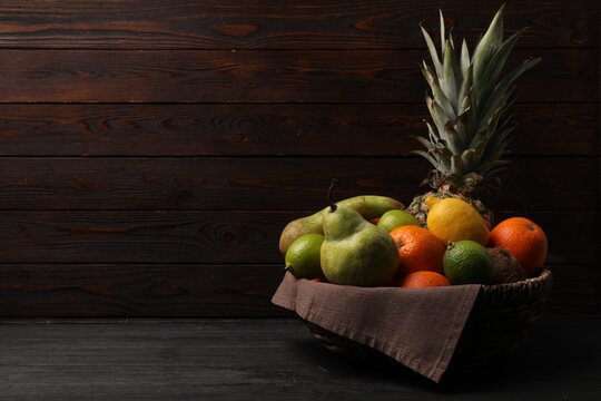 Different fresh fruits in wicker basket on black wooden table, space for text