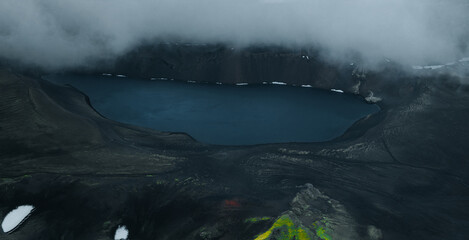 Panoramic view of Ljótipollur crater lake in Iceland's Highlands, surrounded by dark volcanic slopes beneath dramatic storm clouds. A remote and breathtaking volcanic landscape. © Jag_cz