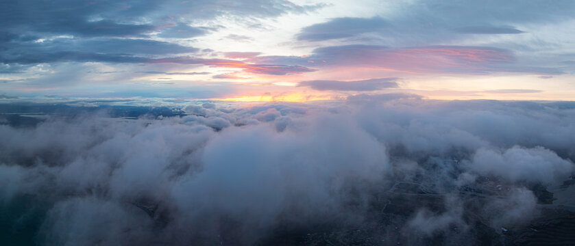 Aerial view above dramatic clouds in the Icelandic highlands at sunset, with soft golden light, misty valleys and a vast remote landscape hidden beneath the clouds.
