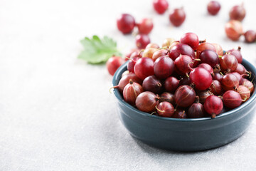 Fresh red gooseberries in bowl on light grey table, closeup. Space for text © New Africa