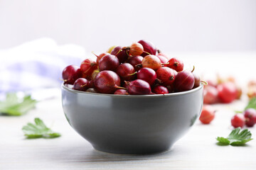 Fresh red gooseberries in bowl and green leaves on wooden table, closeup © New Africa