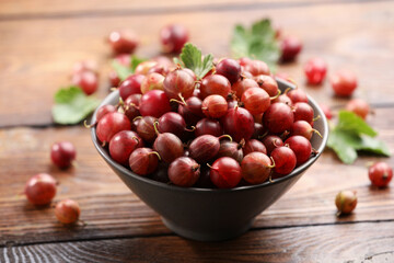 Fresh red gooseberries in bowl and green leaves on wooden table, closeup © New Africa
