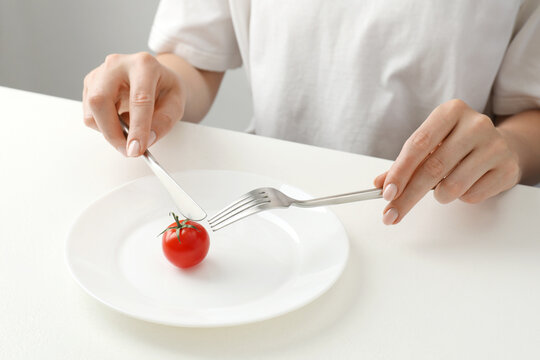 Anorexia concept. Woman refusing plate with tomato at white table, closeup