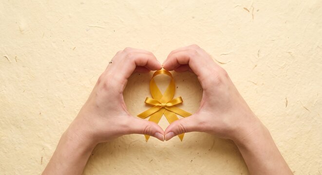 Hands forming a heart shape around a gold awareness ribbon