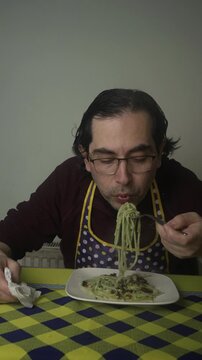 Medium Vertical Shot of Man Eating Creamy Green Fettuccine Pasta, Man wearing Apron Eating Homemade Avocado Fettuccine at Table