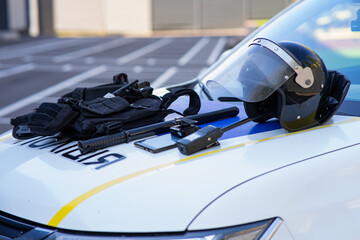Police tactical equipment including a riot helmet, baton, and vest laid on the hood of a patrol car. © TetianaRUD