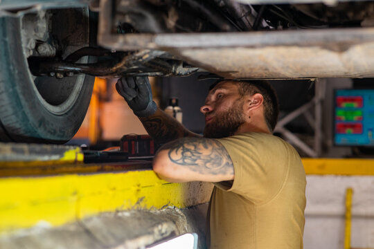 Mechanic working under lifted car in repair shop.