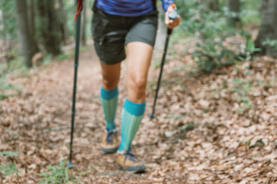Blurred background of a hiker's teal compression socks and boots as trekking poles drive forward on a leaf-covered trail. Adventure concept.