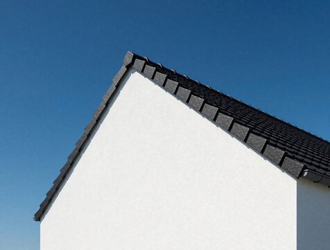 White house gable and dark roof tiles meet under bright blue sky. Clean architectural lines create minimal geometric pattern. Modern residential building exterior detail.