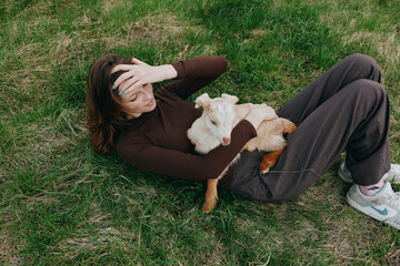 Naklejka premium Relaxed woman lying on grass outdoors with a playful goat kid resting on her chest, sunlit moment, casual clothes, gentle breeze, natural colors, tranquil countryside vibe