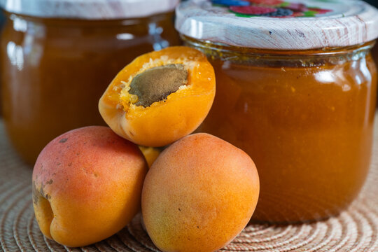 Fresh whole and halved apricots are arranged in front of jars of homemade apricot jam.