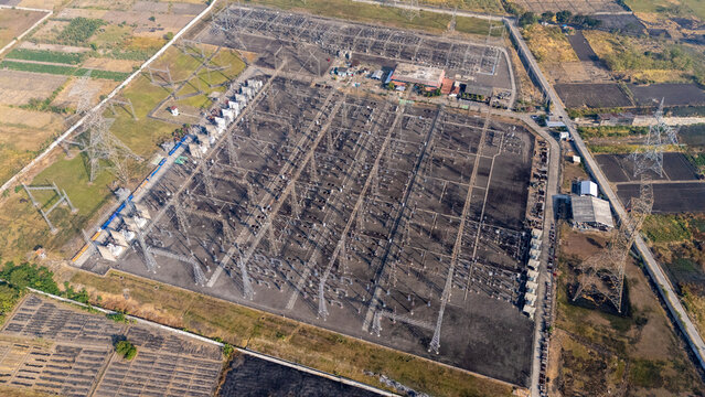 Aerial view of an electrical substation featuring high-voltage power lines, metal towers, and transformers surrounded by agricultural fields in Indonesia.