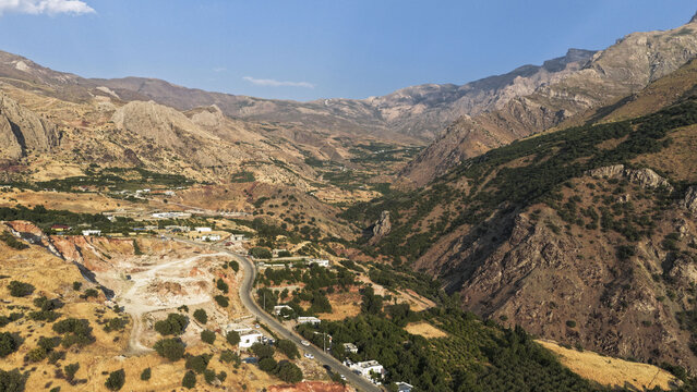 Aerial view of the mountainous landscape of Choman with a winding road, scattered buildings, and lush vegetation in Choman, Erbil Governorate, Iraq.