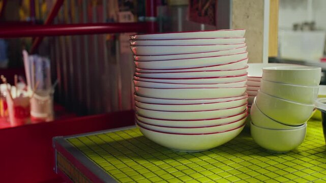 Stacked ceramic bowls with red rims sitting on yellow counter in Asian restaurant kitchen. Footage is perfect for food service marketing, restaurant promos, or culinary business videos