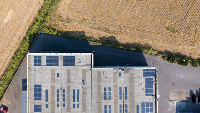 Aerial view of a specialty coatings manufacturing facility featuring rows of rooftop solar panels, surrounded by agricultural fields in an industrial area, Milan, Lombardy, Italy.