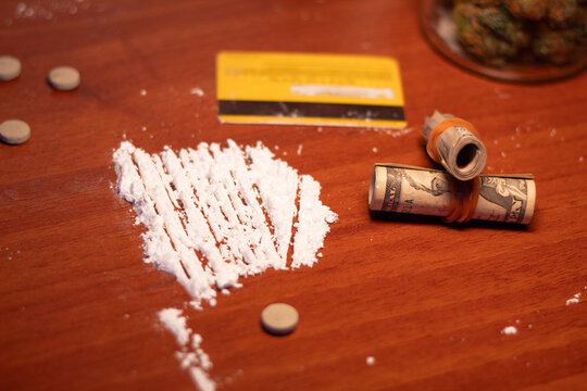 Visual depiction of drug use featuring cocaine, cannabis, pills, and money on a table