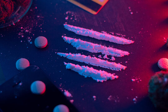 Conceptual scene of drugs in a nighttime party setting with cocaine and pills under neon lighting