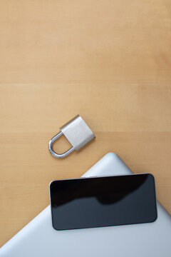 Vertical smartphone on closed laptop with padlock on wooden desk