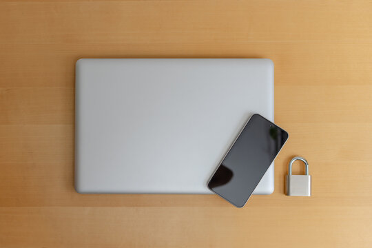 Smartphone on closed laptop with padlock on wooden desk