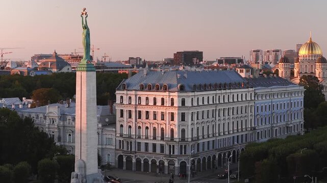 An aerial perspective shows the Freedom Monument, classic architecture, and the Nativity Cathedral dome under warm sunset light in Riga, Latvia.