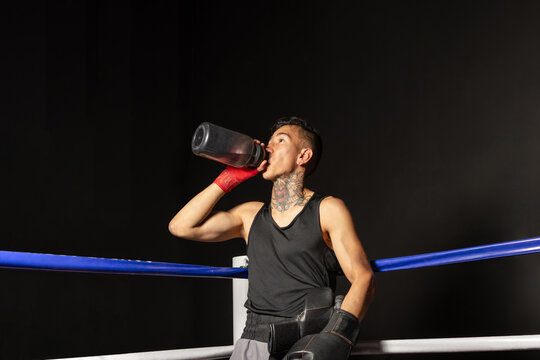 Calm Hispanic boxer standing in boxing ring corner against dark background
