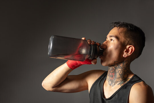 Close up hispanic boxer drinking water from reusable bottle against dark background
