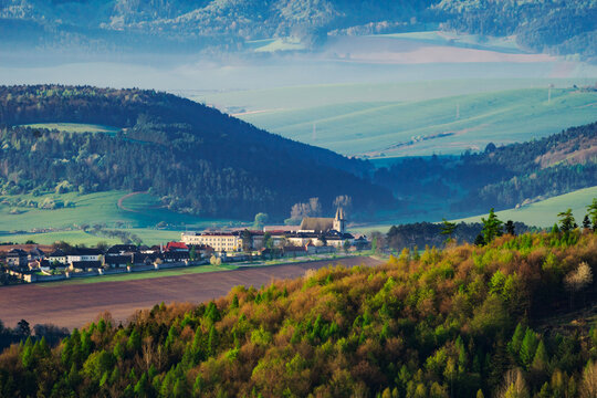 Aerial view of the historic Spisska Kapitula ecclesiastical complex nestled among rolling green hills and forests in the morning mist in Levoca, Presovsky kraj, Slovakia.