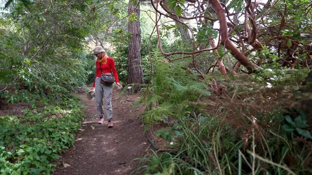 A senior woman walks through the Mendocino Coastal Botanical Gardens in Fort Bragg, California, looking at the various plants and flowers.