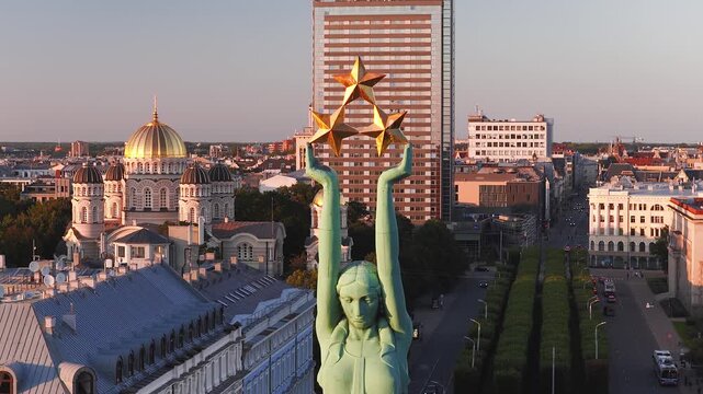 Aerial view of the Freedom Monument holding three golden stars above the Riga cityscape with the Nativity of Christ Cathedral in Latvia at sunset.