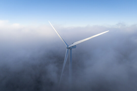 Aerial view of Windpark Freilanderalm wind turbine rising above a thick layer of clouds under a clear blue sky in Hebalm, Styria, Austria.