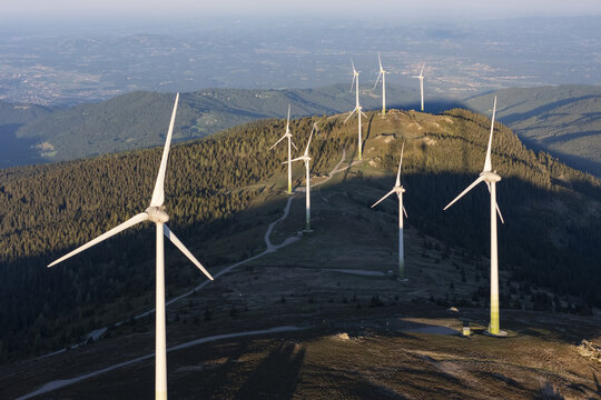 Aerial view of Windpark Handalm with wind turbines standing on a mountain ridge surrounded by pine forests in the golden hour light in Weinebene, Steiermark, Austria.