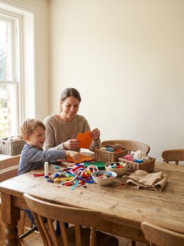 Happy mother and little son making a DIY Halloween costume together with craft materials on a wooden table at home