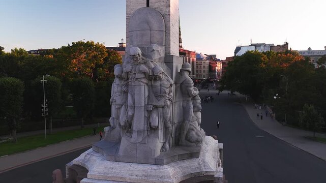 Aerial view showing the detailed granite sculptures carved on the base of the Freedom Monument during sunset in Riga, Latvia.