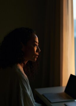 Young woman sitting at a desk with a laptop in front of her. she is facing away from the camera, with her head tilted slightly to the side.