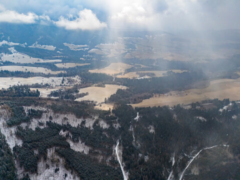 Aerial view of the snow-covered Polana mountains with sunbeams breaking through clouds over forests and fields in Lubietova, Banska Bystrica Regio, Slovakia.