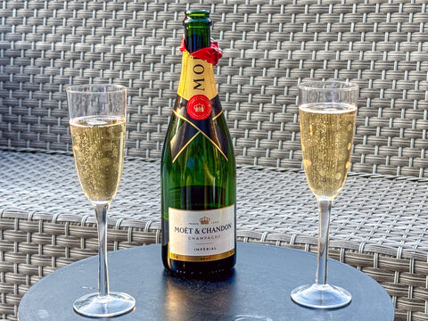Cardiff, Wales, UK - 12 August 2026: Open bottle of Moet et Chandon champagne and two full flute glasses on a table on a garden patio.